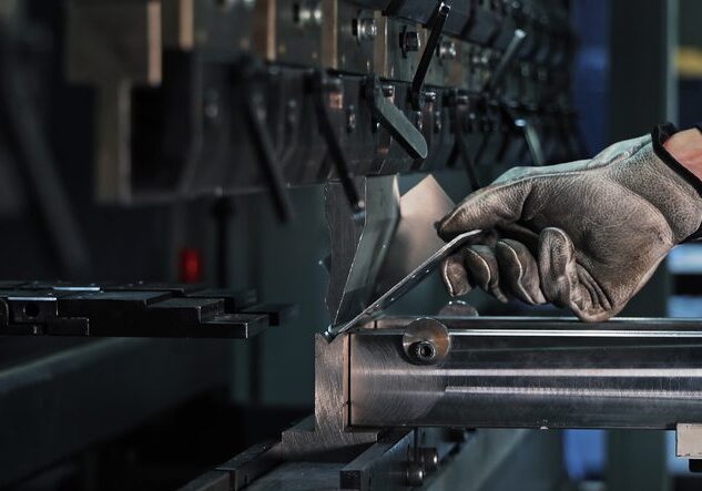 Sheet metal bending on CNC machine. Gloved worker bending a metal sheet using a CNC press brake in an industrial setting focused on precision manufacturing